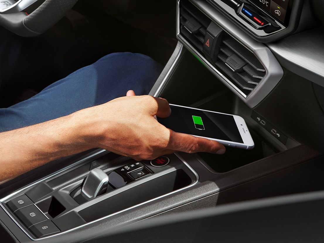 Detailansicht der Induktionsschale zum kabellosen Laden eines Smartphones im SEAT Leon 5-Türer und SEAT Leon SP Kombi. Eine Person legt gerade ein Smartphone zum Laden hinein.